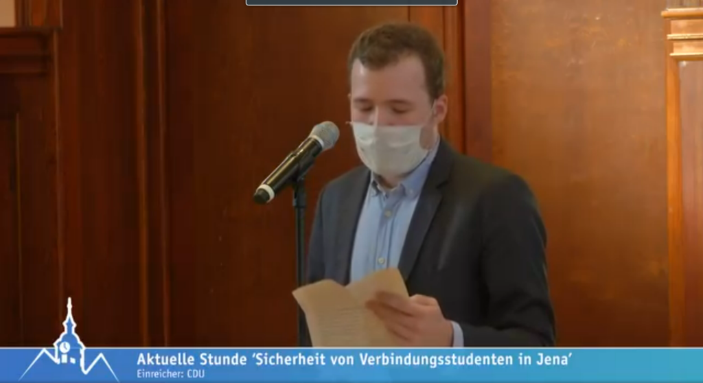 Foto von Benedikt Kern-Wagner vorm Mikro mit Text in der Hand. Am Bildrand unten steht "Aktuelle Stunde "Sicherheit von Verbindungsstudenten in Jena"