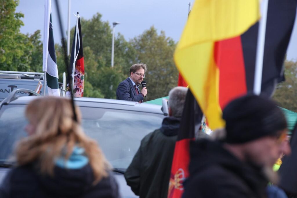 Foto auf dem Peter Schreiber am 03.10.2024 in Gera auf einer Bühne mit einem Mikrofon zu sehen ist.