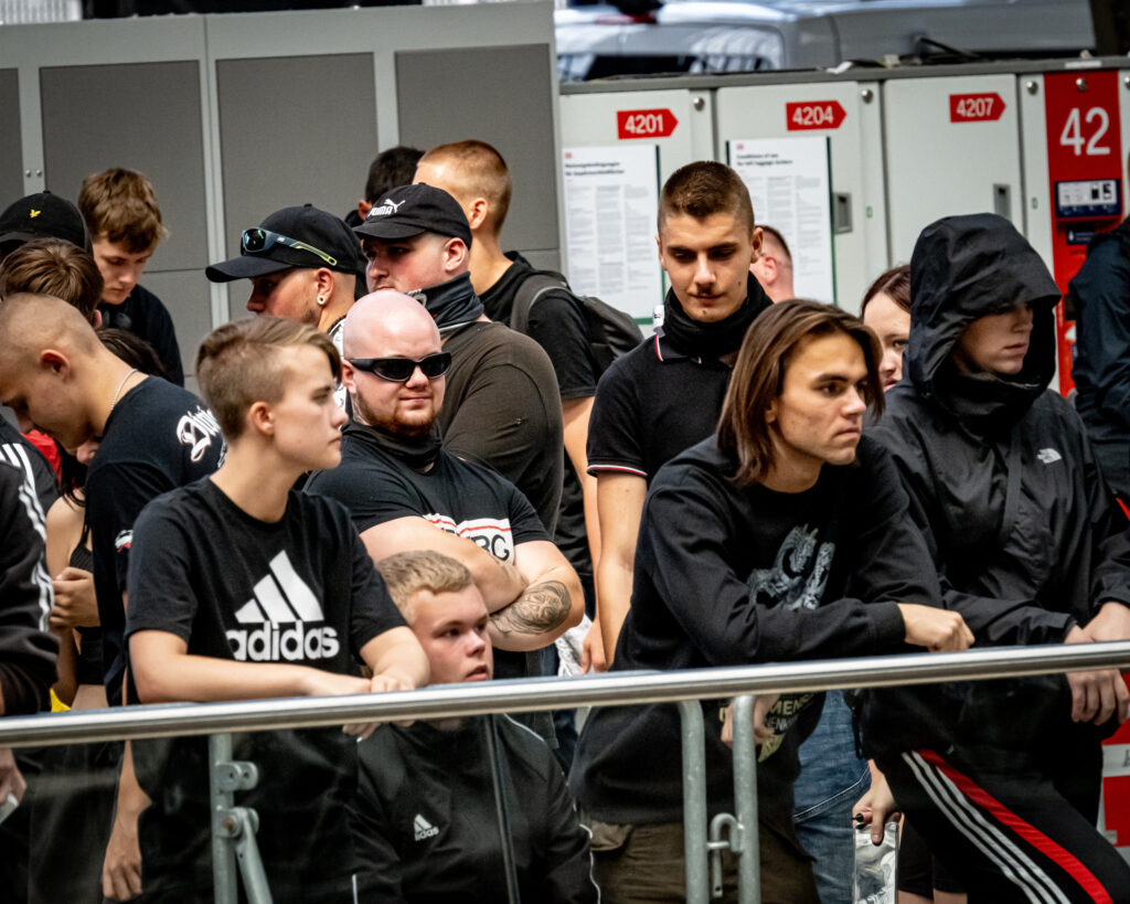 Man sieht junge Rechte an ein Geländer im Leipziger Hauptbahnhof gelehnt. Caroline Hein trägt halbseitig abrasierte Haare und ein dunkles Adidas-Shirt.