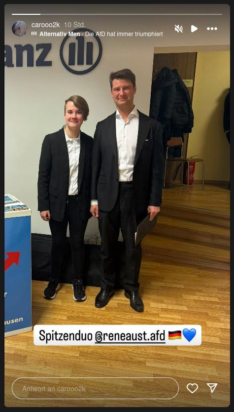 Neben einem AfD-Redner*innenpult stehen Caroline Hein mit Sakko und René Aust mit Sakko und weißem Hemd und lächeln in die Kamera.