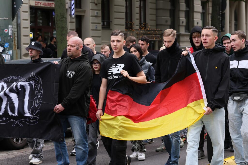 Foto des queerfeindlichen Aufmarschs am 23.08.2025 in Magdeburg auf dem Justin Eibel und Anthony Scholz zu sehen sind. Die beiden tragen gemeinsam eine schwarz-rot-goldene Fahne.