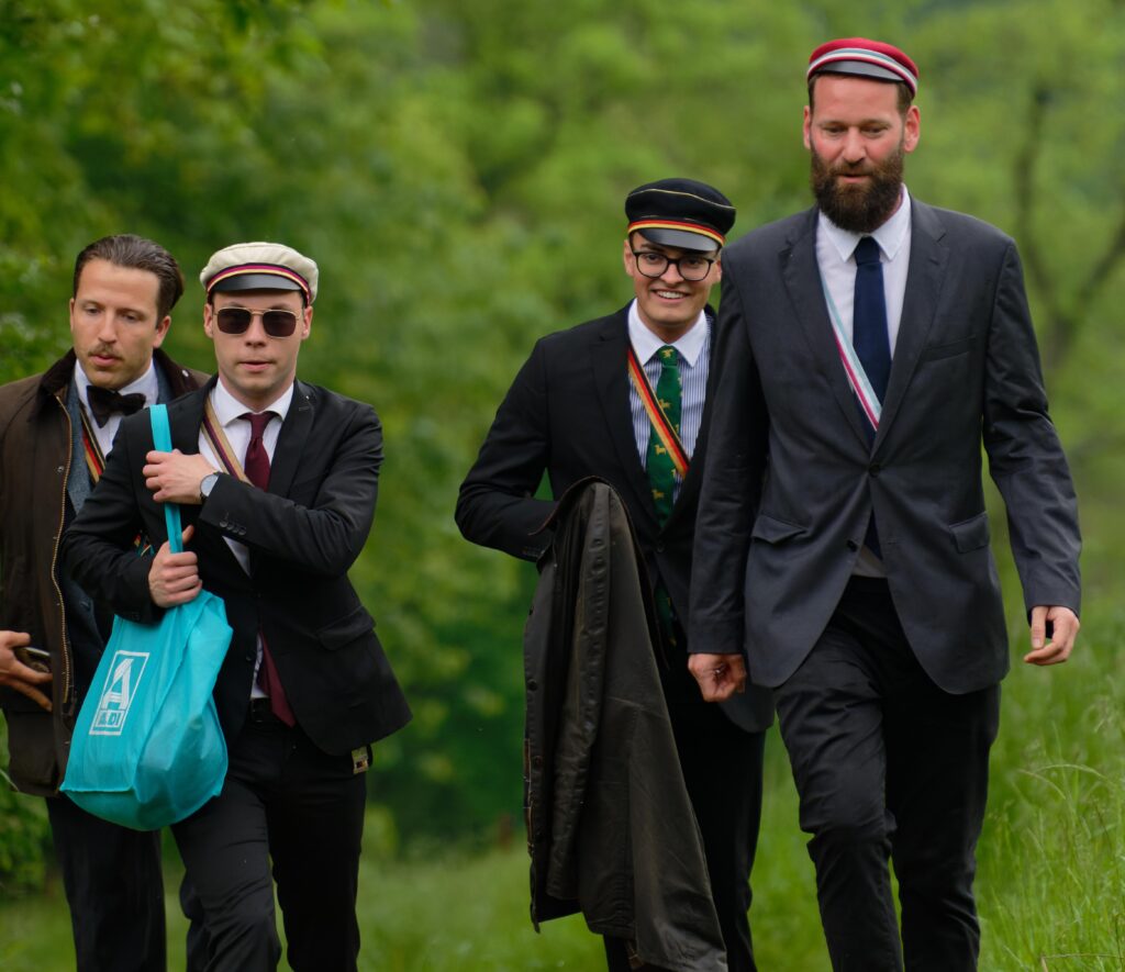 Foto von Henning Eggers und drei weiteren Burschenschaftern in Couleur bei der Ankunft zum DB-Burschentag. Eggers trägt Couleur der Burschenschaft Germania Jena und trägt einen großen blauen Aldi-Beutel über der Schulter.