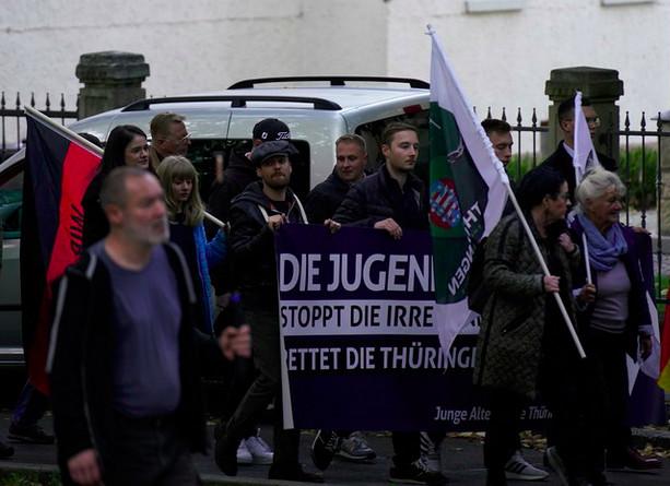 Foto von mehreren Personen auf einer Demonstration. Die Personen vorne tragen Fahnen von "Freies Thüringen", dahinter tragen mehrere Personen ein Transparent der "Jungen Alternative".