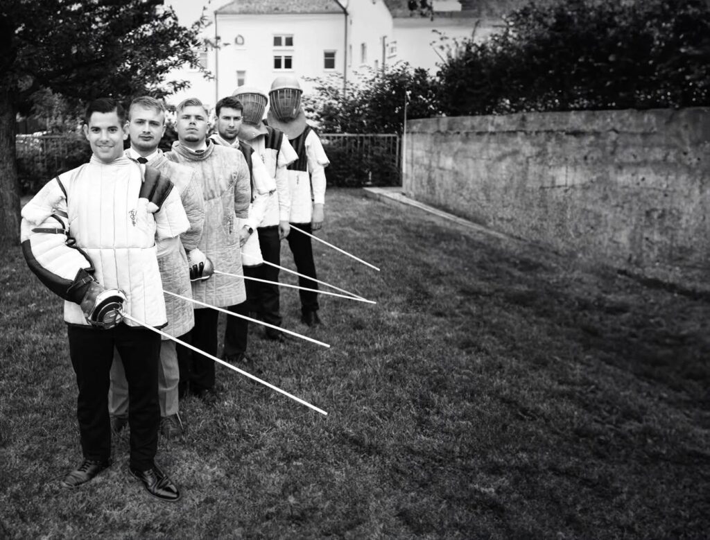 Foto in schwarze-weiß von Florian Ockenfels (2.v.l.) sowie u.a. Tim Beutler und Alexander Claus in Germania Fechtmontur. Alle tragen Fecht-Ausrüstung und einen Säbel in der rechten Hand.