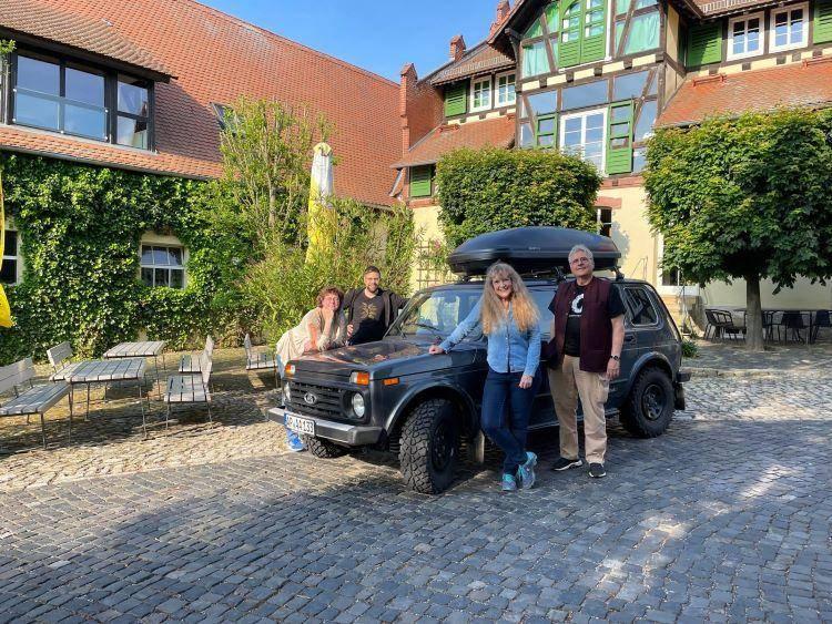 Im Innenhof des Schloss Auerstedt stehen lächelnd Marion Schneider, Klaus Böhm-Schneider, Ivana Steinigk und Silvan Haselbach bei Sommerwetter rund um einen Lada Niva mit Dachbox.